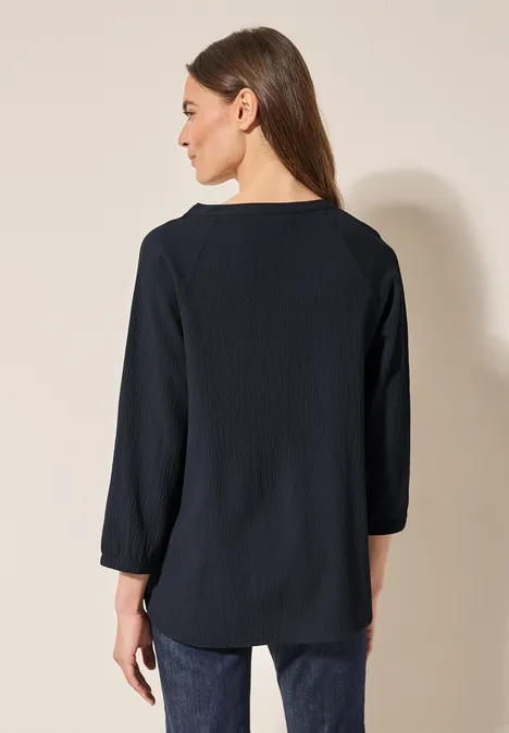 Frau mit langen Haaren trägt dunkle Bluse und Jeans, von hinten fotografiert.